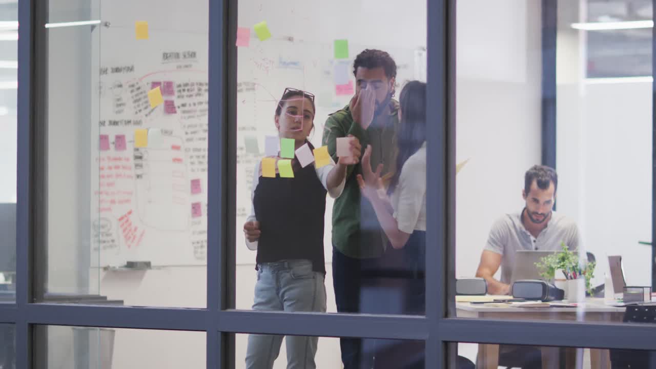 Gruppo eterogeneo di colleghi di lavoro che fanno brainstorming utilizzando una parete di vetro in sala riunioni.
