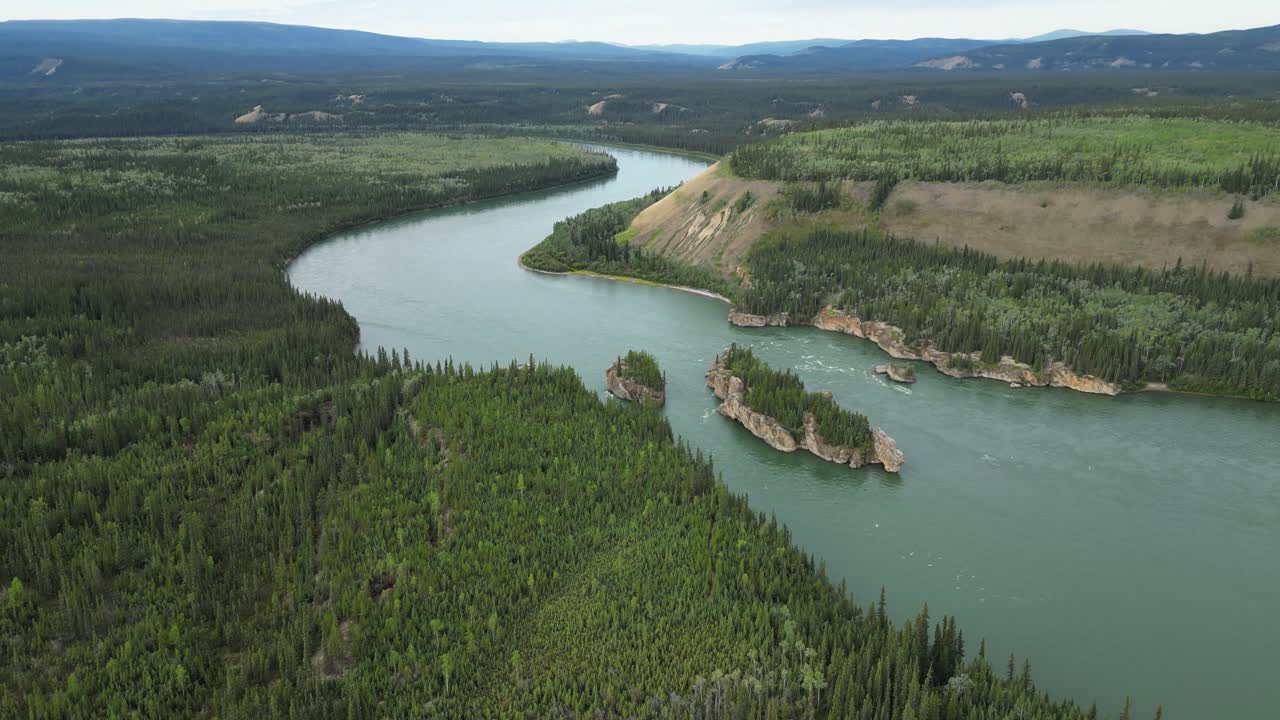 En drone flyver baglæns fra Five Finger Rapids i Yukon, Canada, og vippes op for at vise den bugtende Yukon-flod, strømhvirvler, omkringliggende skov og fjerne bjerge i et bredt luftfoto