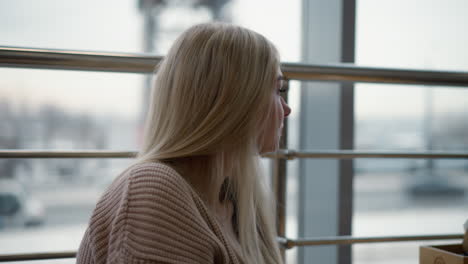 side view of lady enjoying breakfast with a cup in hand, blurred moving car and urban scenery visible through large glass window, casual moment in a modern cafe setting