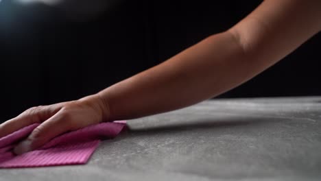 woman wipes grey table clean with soapy water and pink cloth, black background