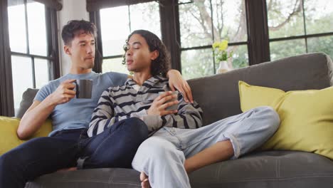 Feliz-Pareja-Masculina-Diversa-Sentada-En-El-Sofá-Y-Tomando-Café-En-La-Sala-De-Estar