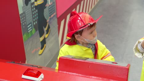 adorable niño multiétnico coreano-ucraniano que finge ser bombero con un casco de seguridad rojo brillante y uniforme