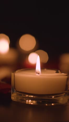 vertical video close up of romantic lit red and white candles burning on black background with bokeh lighting 5