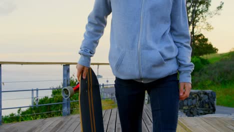 Front-view-of-young-caucasian-female-skateboarder-walking-with-skateboard-at-observation-point-4k