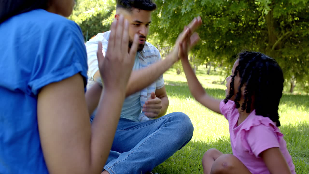 Family enjoying clapping game together in sunny park, smiling and bonding