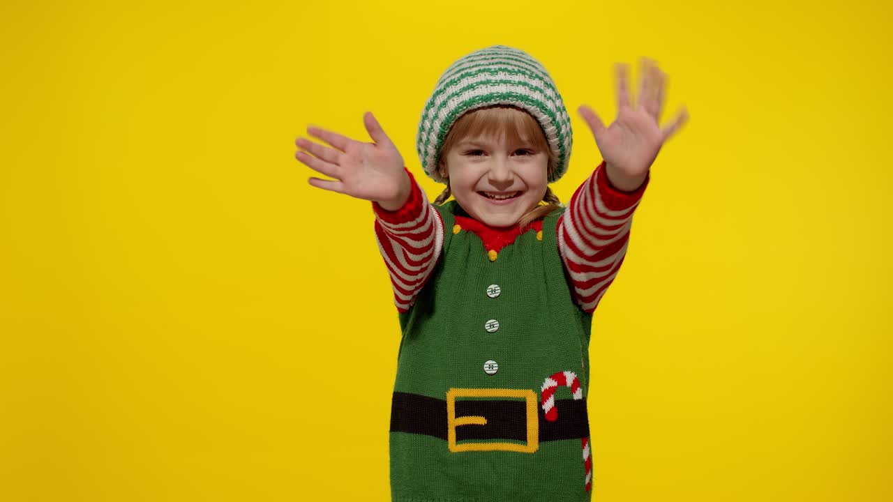 Dívka v kostýmu vánočního skřítka, pomocníka Santy, mává na pozdrav rukou. Ahoj, nazdar, gesto pozdravu.