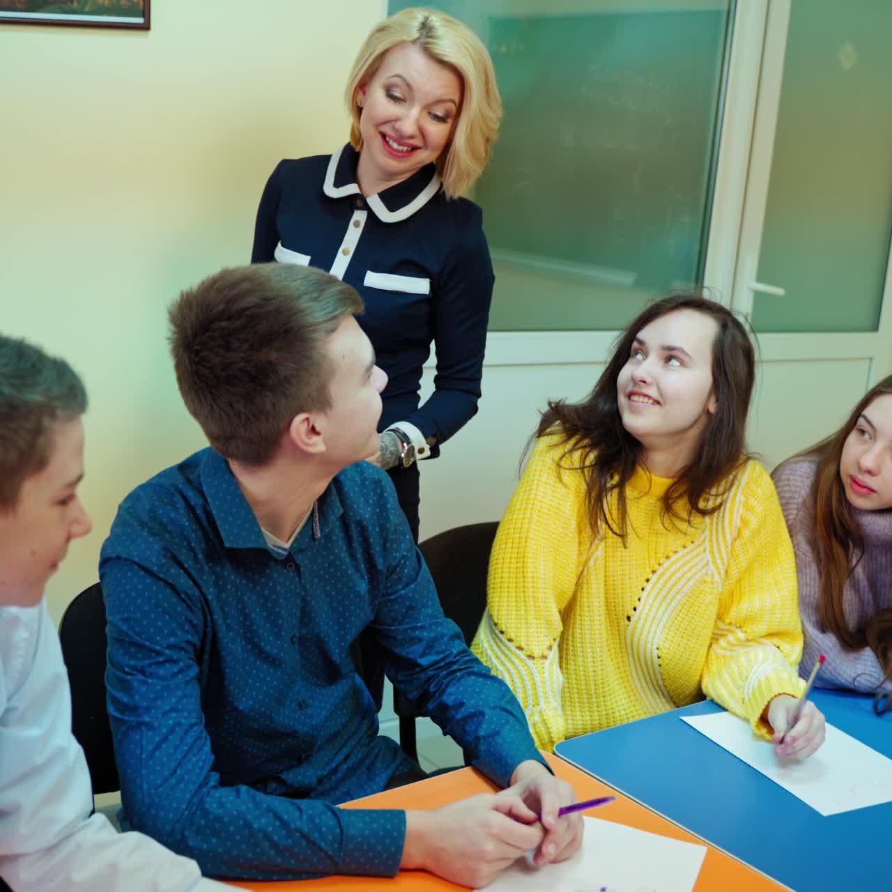 Learning process in middle school. Teen students sitting in the classroom. Positive teacher talking to a boy student. Education concept.
