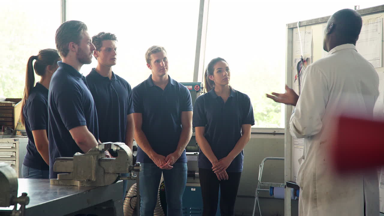 튜터 가 훈련생 엔지니어 들 과 기술 도면 을 논의 하고 있다