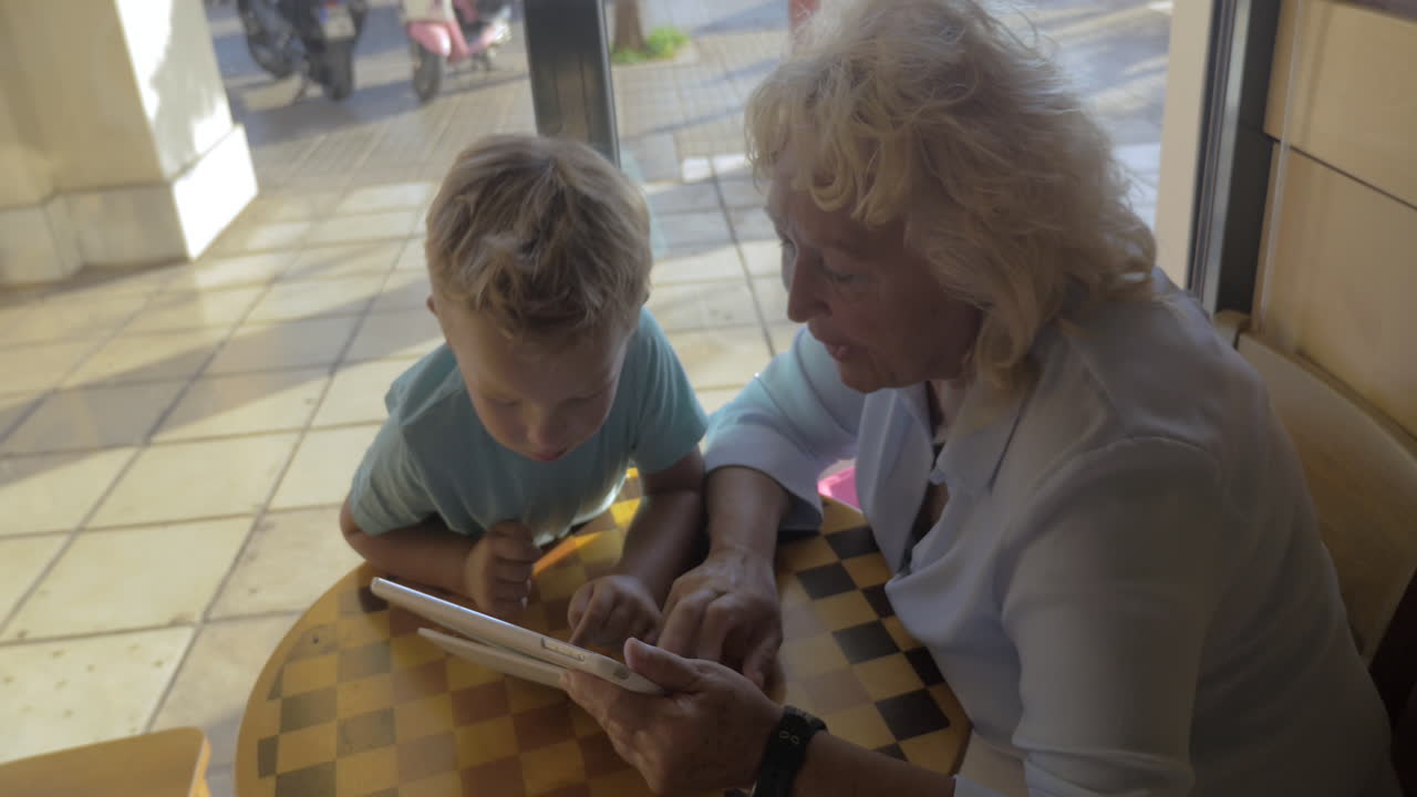 niño y abuela usando una tableta en un café