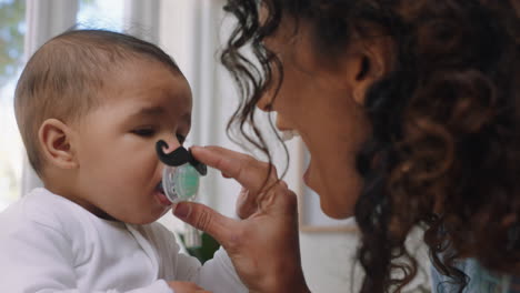 funny baby with moustache pacifier happy mother having fun with toddler at home enjoying silly humor with child sucking on dummy