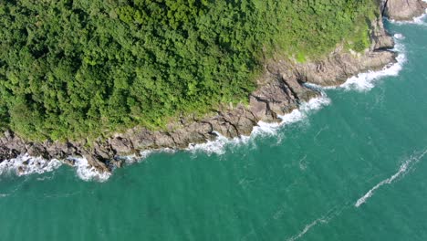 Aerial-view-of-a-jagged-rock-island,-surrounded-with-lush-green-nature-and-Hong-Kong-bay-water