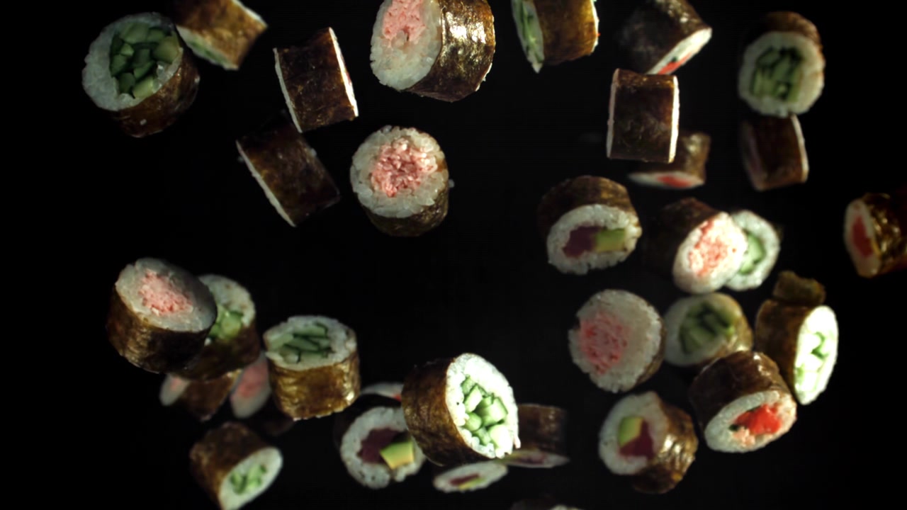 Vari roll di sushi che cadono al rallentatore su sfondo nero