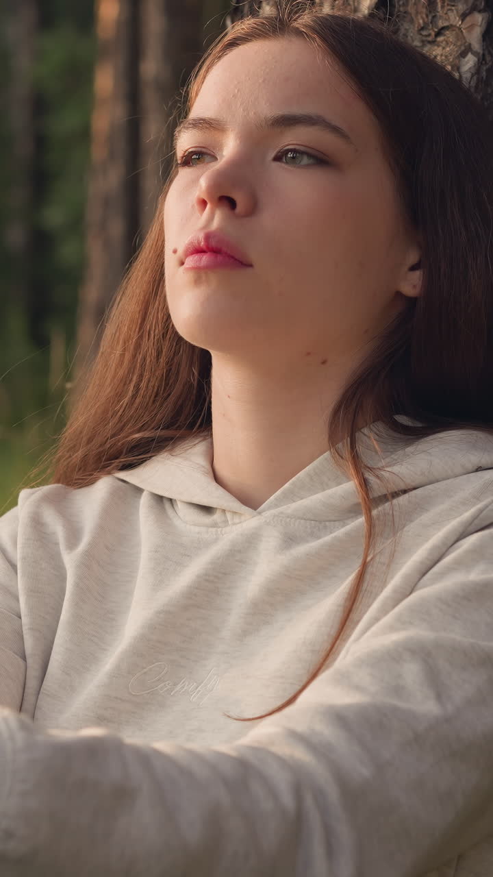 la mujer piensa sentada junto a un árbol en el bosque. los rayos del sol caen sobre la mujer deprimida descansando cerca del tronco de la planta rodeada de naturaleza salvaje. actitud pesimista hacia la vida.