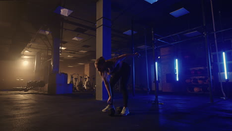 in slow motion a woman lifts a dumbbell over her head while working out in a dark gym. athletic strong woman performs a difficult workout with lifting dumbbells