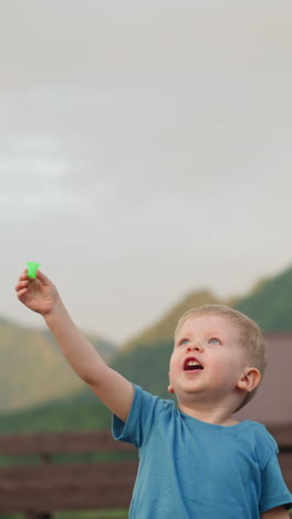 excited toddler boy launches flying toy playing on ground with benches at highland eco resort against distant sunny mountains slow motion