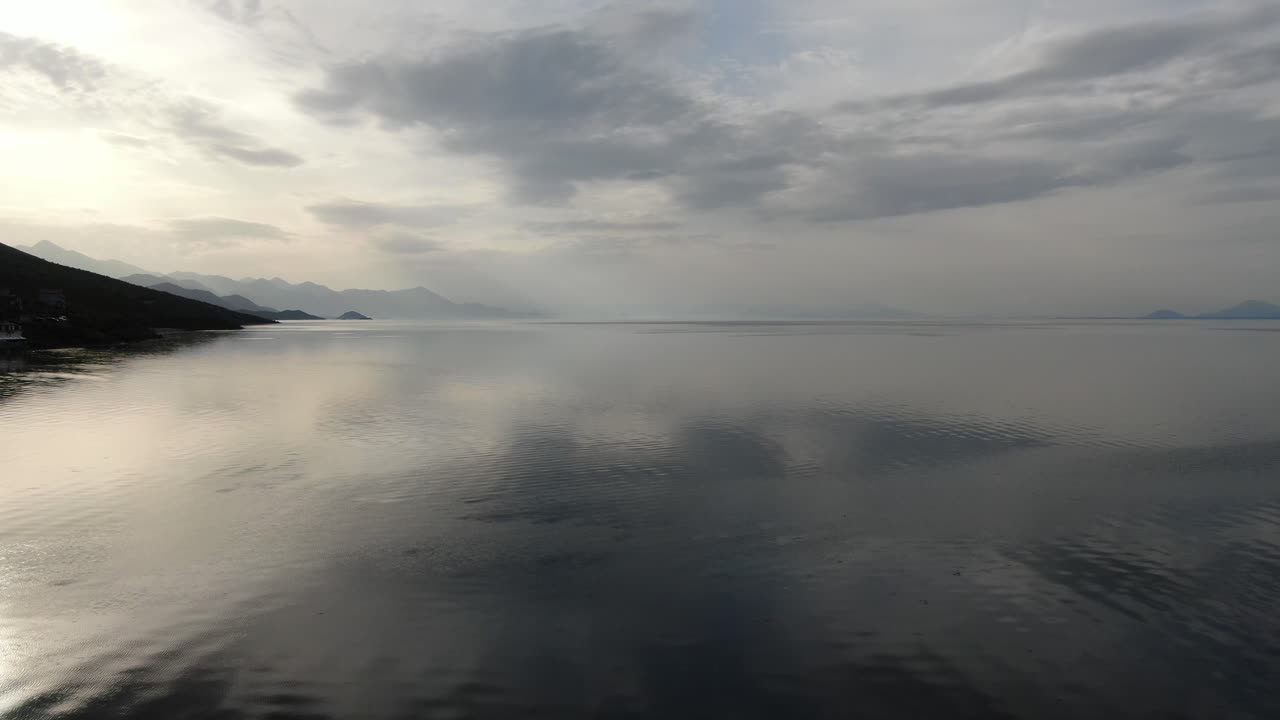 Drone view in Albania flying over Shkod&euml;r lake in Pogradec on cloudy day with shadowy mountains in the horizon