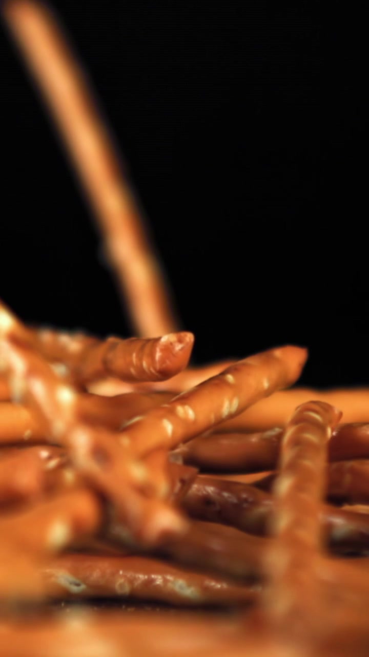 Bastoncini di pretzel dorati che cadono al rallentatore su sfondo nero