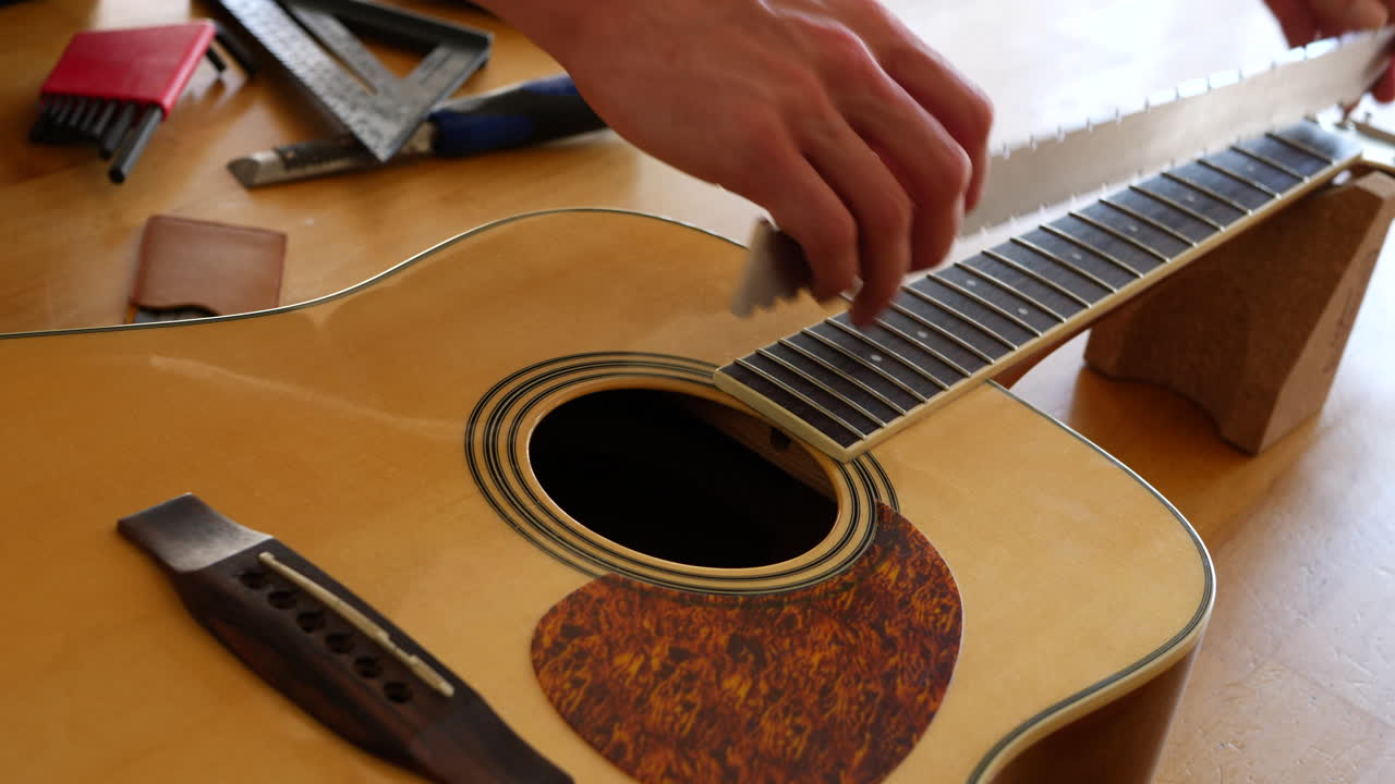 Close up hands of a luthier craftsman measuring an acoustic guitar neck fretboard on a wood workshop bench with lutherie tools SLIDE RIGHT
