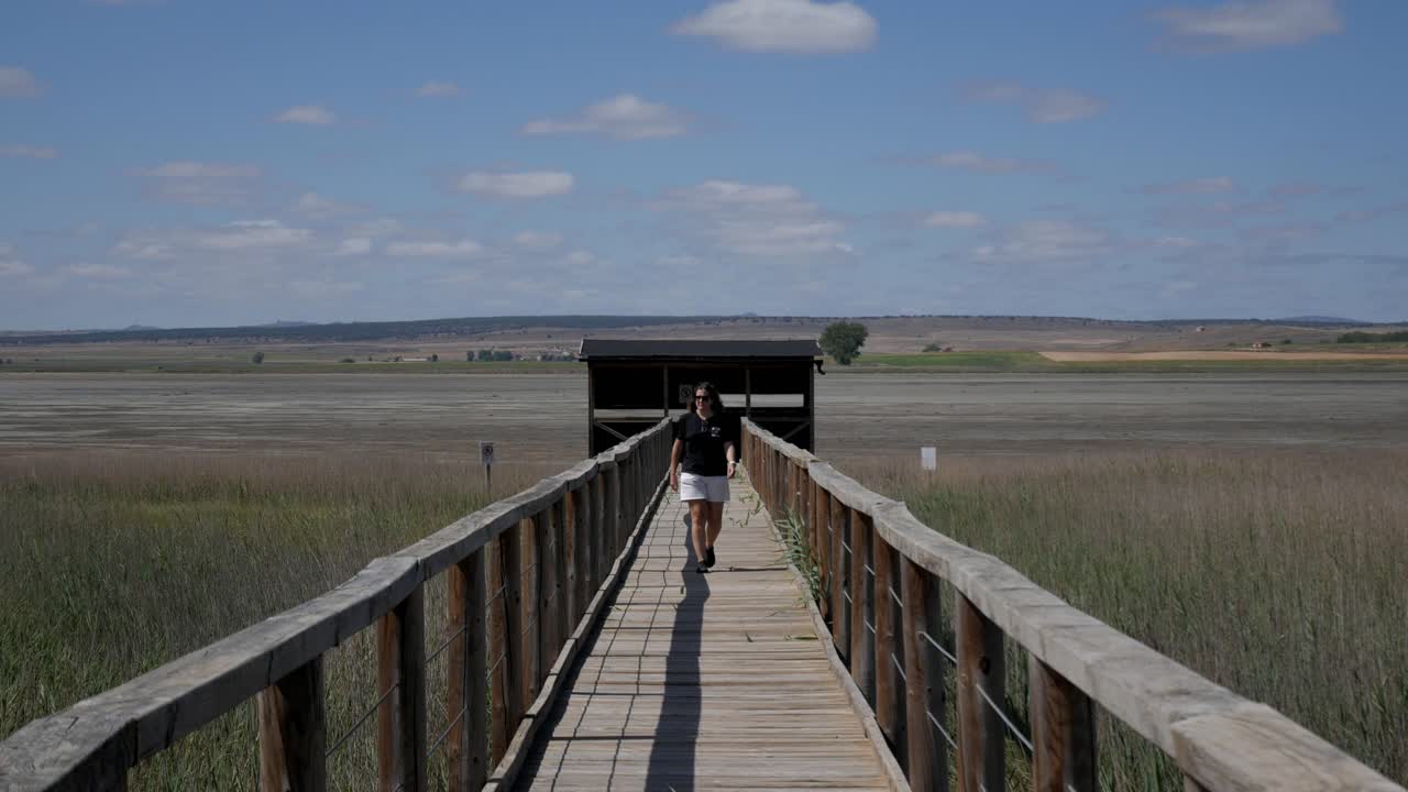 A person walking on a wooden path leading into a scenic natural reserve