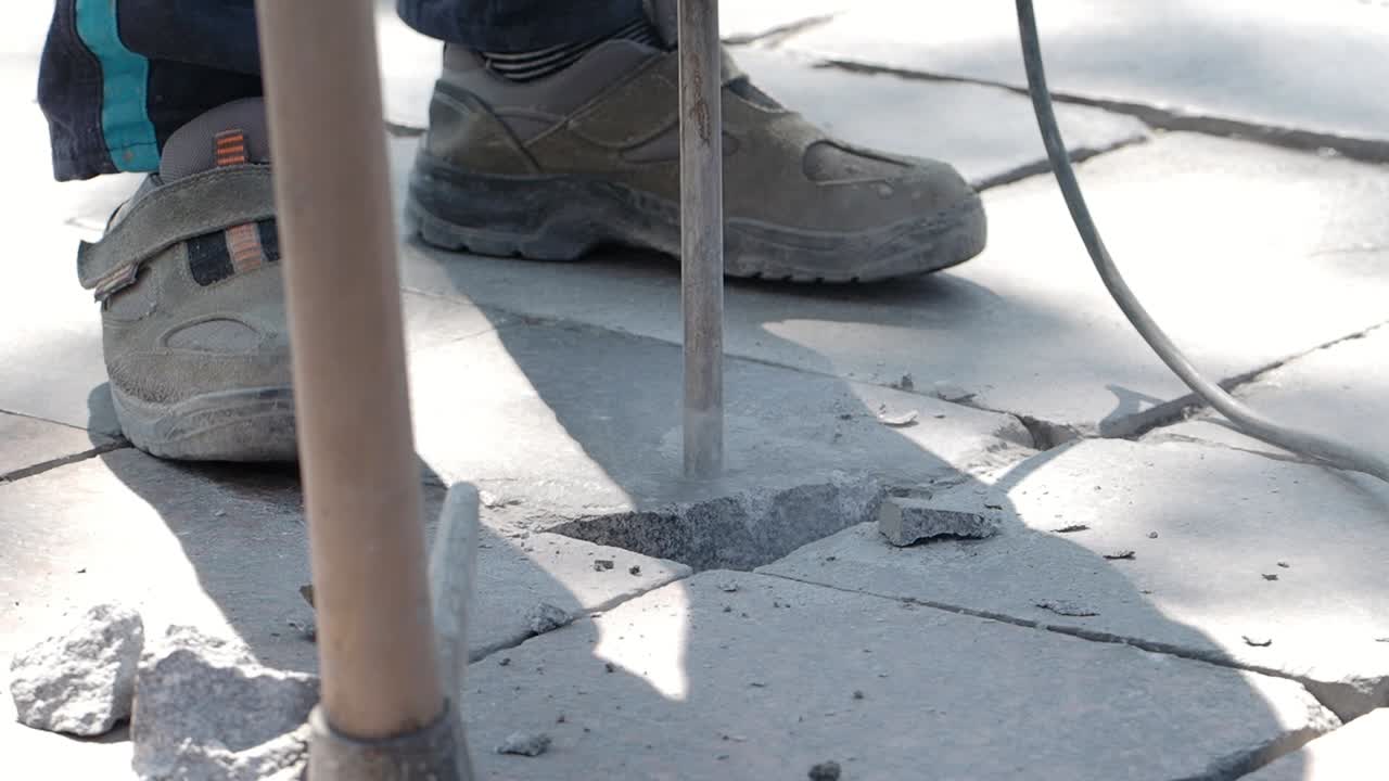 Worker using jackhammer to break paving stones