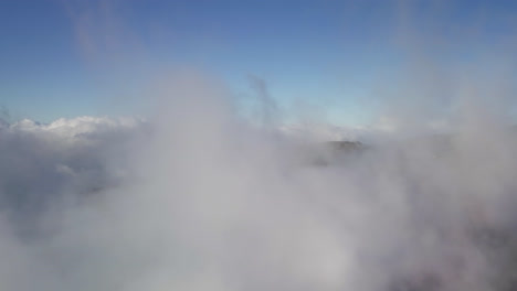 Soar-though-wispy-grey-stratus-clouds-under-a-beautiful-blue-sky,-aerial-dolly