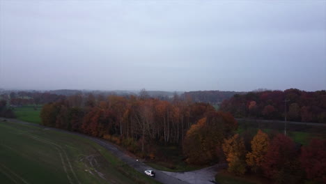 Landende-Drohnenaufnahme,-Die-Eine-Person-Allein-Mit-Dem-Auto-Im-Herbstwald-Zeigt,-Weitwinkelaufnahme