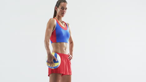 athletic young caucasian woman holding a volleyball poses confidently on a white background, with co