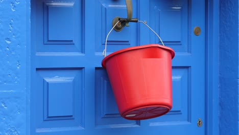 red plastic bucket hanging from a blue door