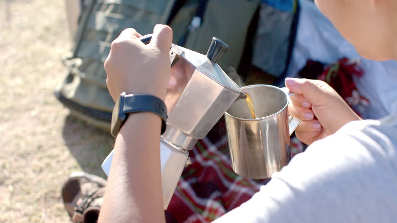 Pouring coffee from moka pot into metal cup during mountain hike