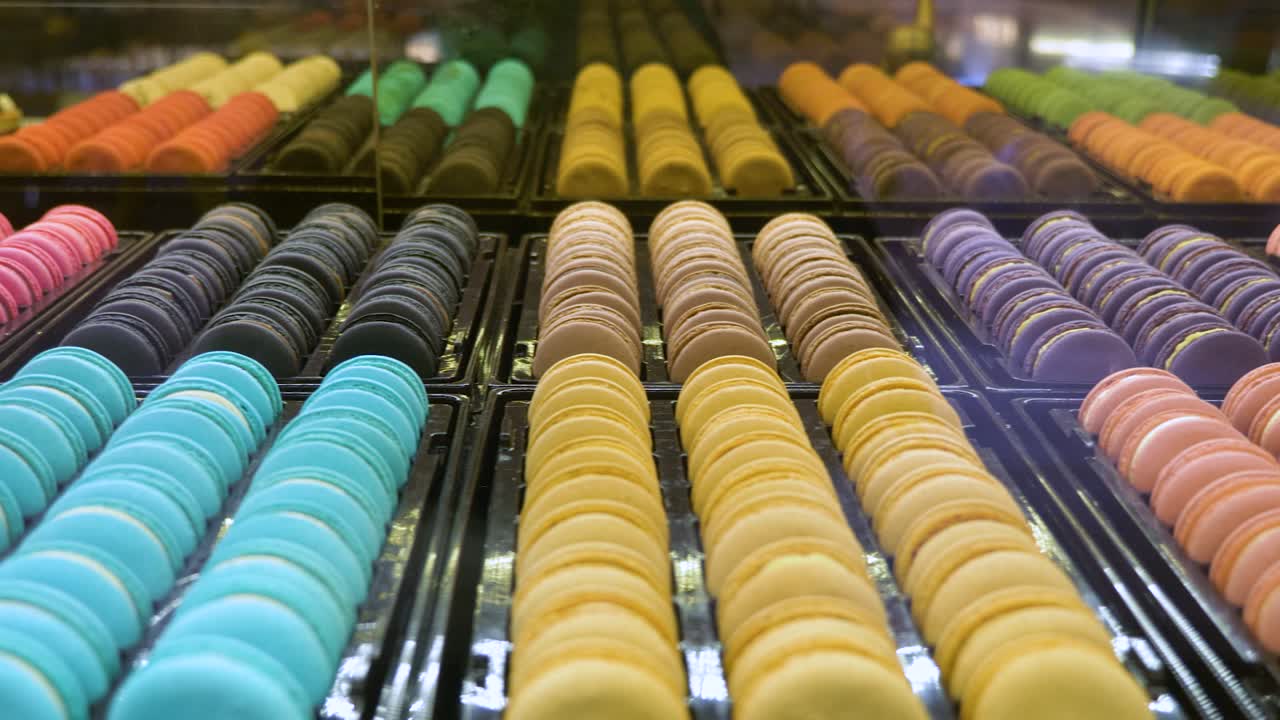 toma panorámica a través de filas coloridas de dulces de galleta macaroon en la pantalla de la ventana de la tienda