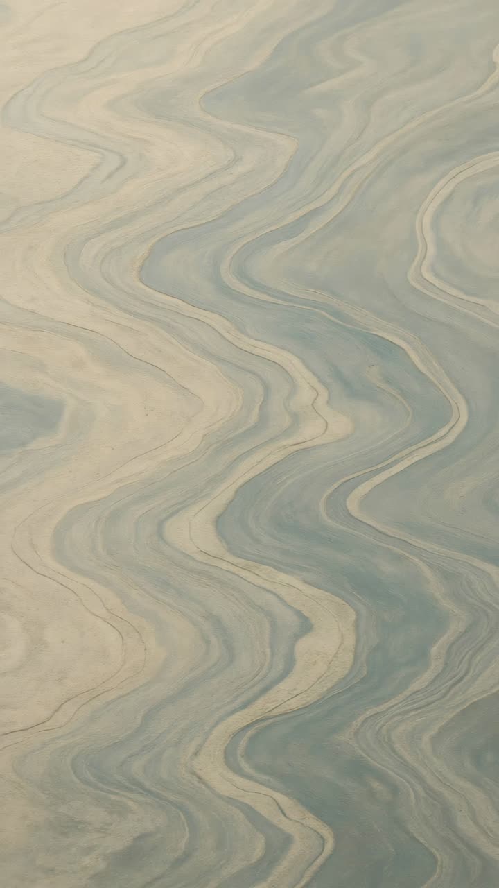Aerial view of swirling blue and beige patterns resembling marbled textures, perfect for a calming