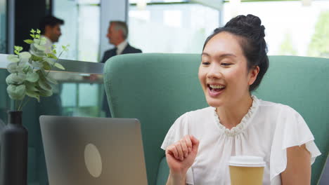 Mujer-De-Negocios-Teniendo-Videollamada-En-Una-Computadora-Portátil-En-La-Mesa-En-El-área-De-Descanso-Del-Edificio-De-Oficinas