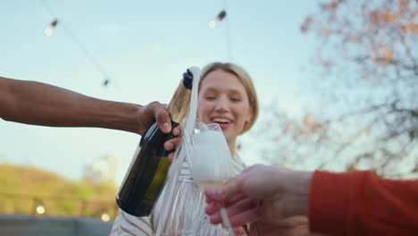 festive man hands opening champagne rooftop close up. friends pouring glasses