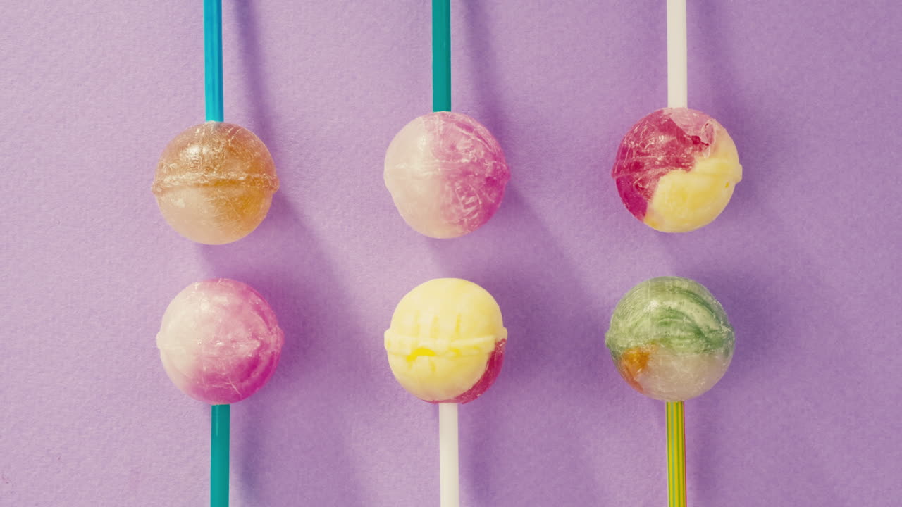 Sweet lollipops with glitter sprinkles on color purple background. Bright texture sugar candies close up top view. Composition of favorite children's summer sweets. Studio shot for shop, supermarket, confectionery