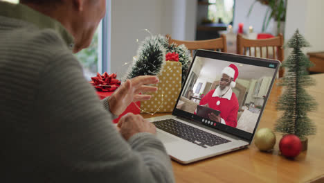 Un-Hombre-Mayor-Caucásico-Teniendo-Una-Videollamada-Navideña-En-Una-Computadora-Portátil-Con-Un-Papá-Noel-Afroamericano-En-La-Pantalla