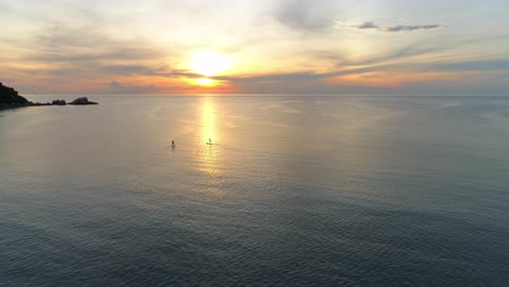 gente remando a la puesta del sol en un océano tranquilo
