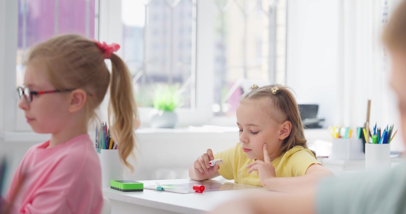 Kleines Mädchen zeichnet mit Filzstift in hellem Klassenzimmer