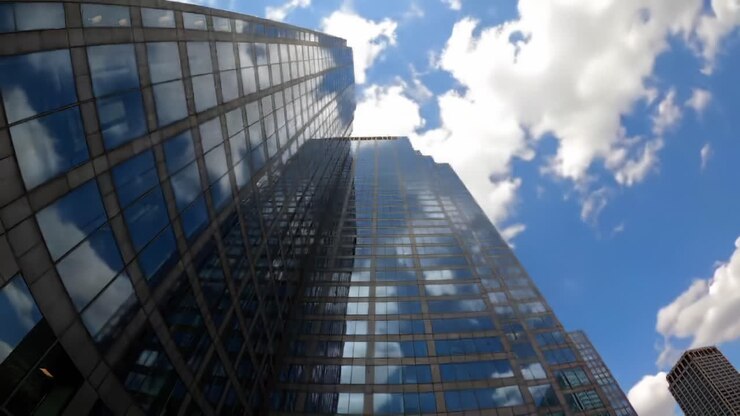Una prospettiva suggestiva di un grattacielo sotto un cielo azzurro con nuvole: catturare il riflesso e l'altezza dell'architettura moderna nei paesaggi urbani.