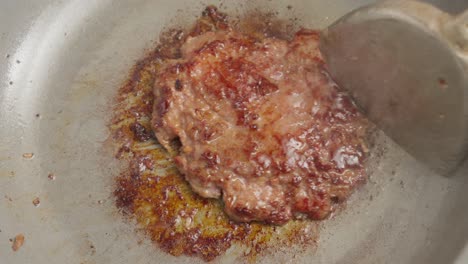 flipping a beef patty in a frying pan with a metal spatula