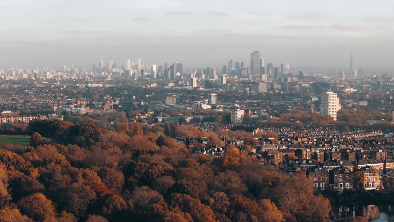 Autumn aerial orbit over Hampstead Heath ponds and London homes with skyline backdrop