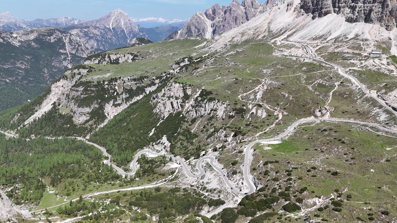 İtalya'nın kuzeyindeki Dolomitler'in kalbinde, ikonik Tre Cime di Lavaredo'ya doğru kıvrılan dramatik dağ yolunda ilerleyen arabaları takip eden sinematik 4K drone görüntüleri.