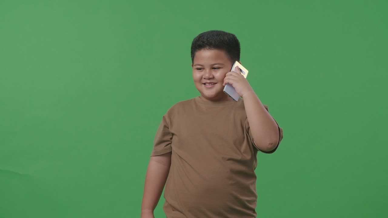 미소 짓는 아시아 소년 이 스튜디오 의 녹색 스크린 에서 휴대 전화 로 이야기 하고 있다