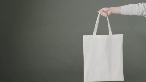 hand of caucasian woman holding white bag on grey background, copy space, slow motion