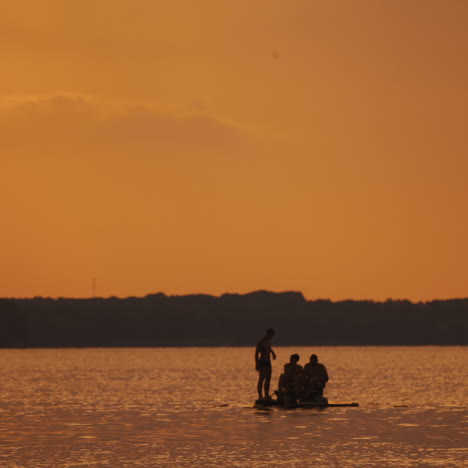 happy men have good time in catamaran at orange sunset. three young guys rafting in catamaran along the river on water in the evening.