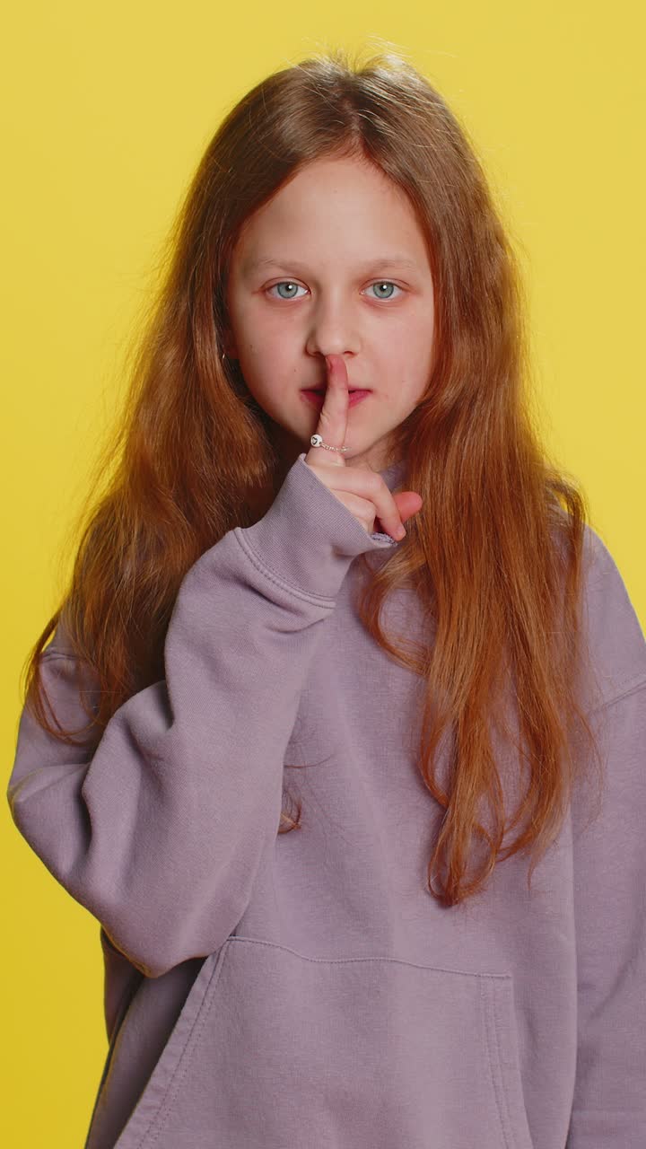 Preteen child girl presses finger to lips makes silence hush sign do not tells gossip secret quiet