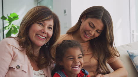 familia hispana de varias generaciones de mujeres en el sofá en casa viendo televisión juntas