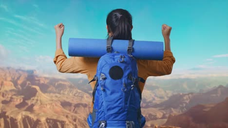 back view of a female hiker with mountaineering backpack screaming goal celebrating the success while traveling at the top of mountain