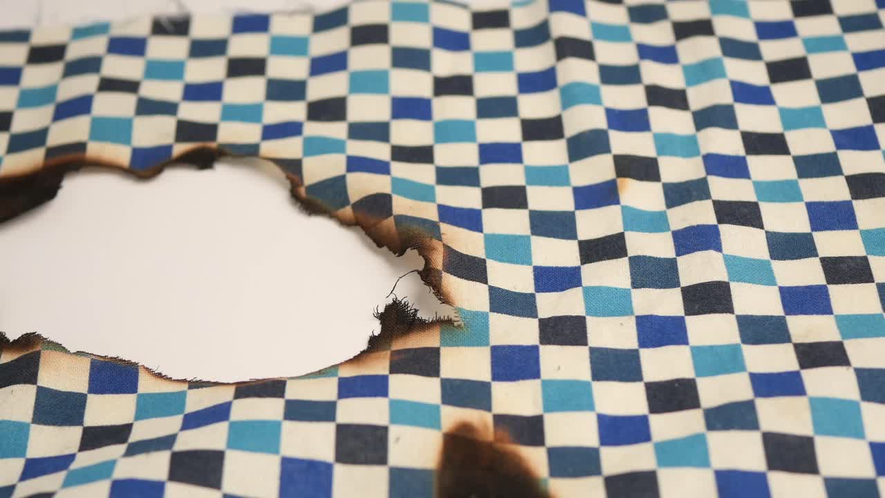 Close-up of Burned Checkered Fabric with a Large Hole