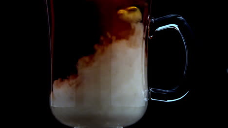 milk pouring into tea in a glass