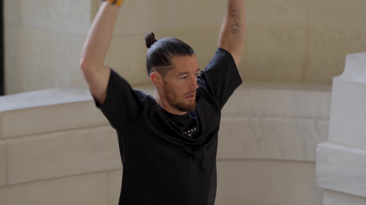 A handsome Caucasian man with his hair tied back in a bun, doing upper-body warm-ups before a sports competition